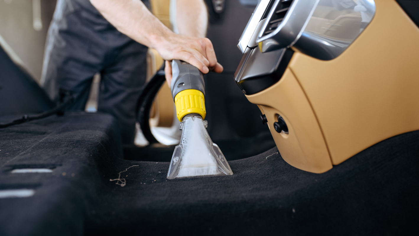 A man is using a vacuum to clean a seat